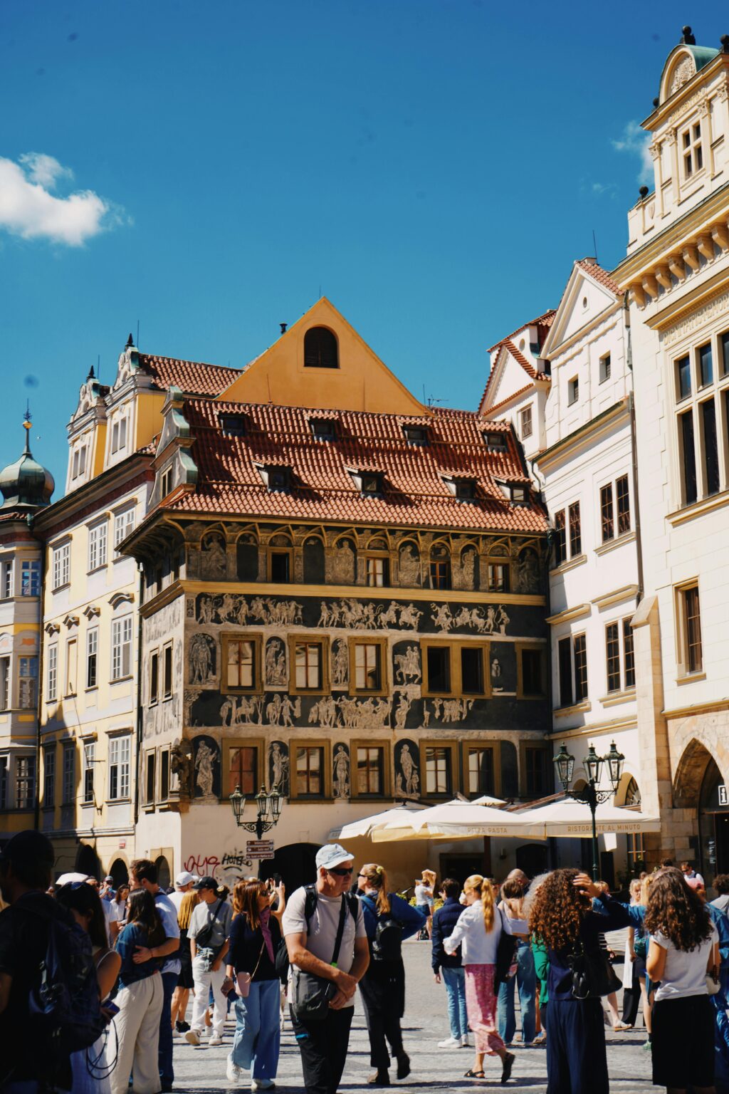 Crowds explore Prague's historic buildings under a clear blue sky.